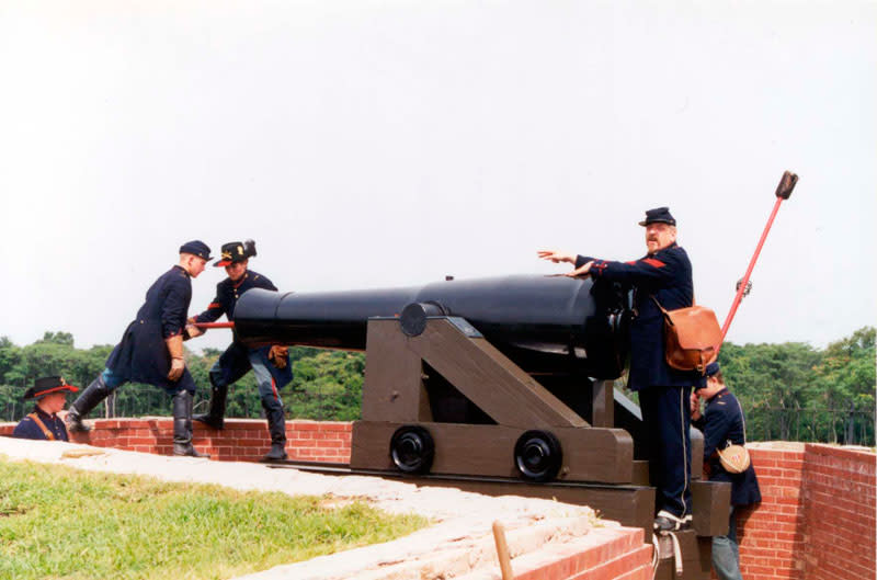 Uniformed Fort Delaware interpreters working around a large mounted cannon